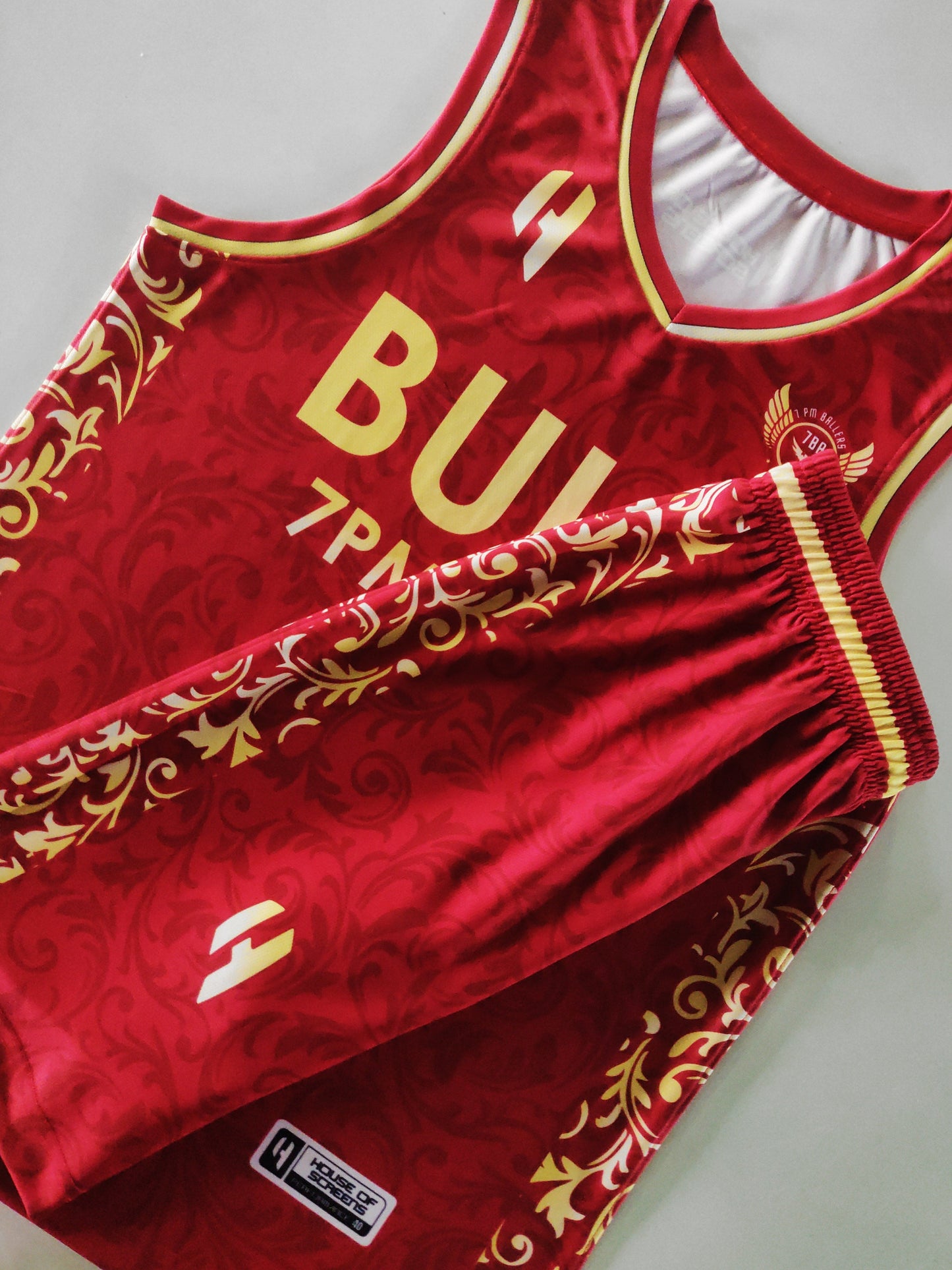 Customizable basketball jersey and shorts set in red and gold colors with abstract patterns and sample text for personalization.